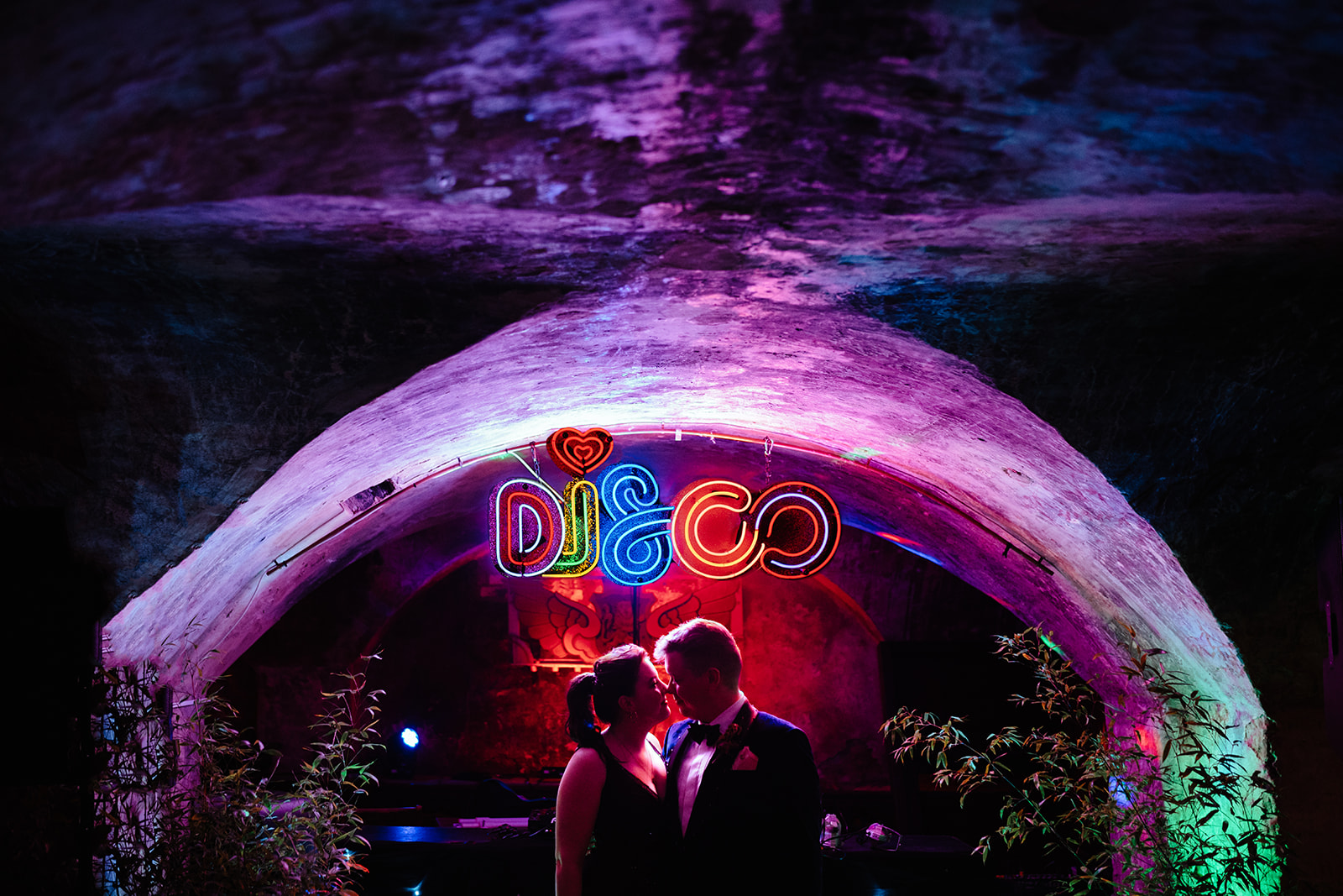 bride & groom in front of neon "disco" sign kissing at Mount without