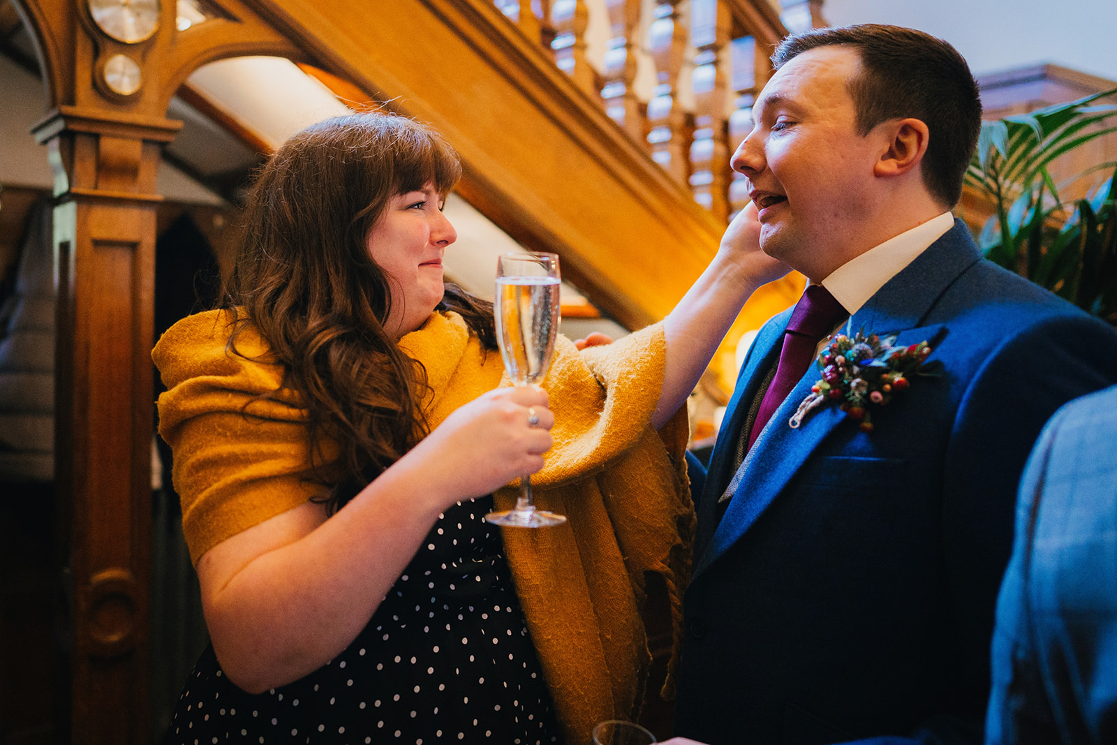 a wedding guest holds a glass of champagne and touches the grooms face, they both look emotional