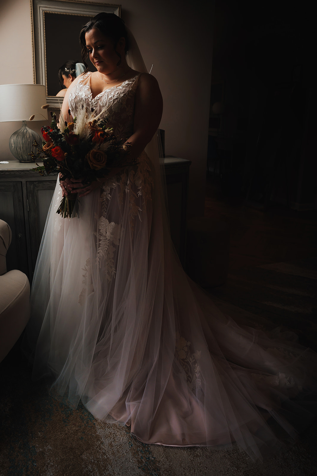 a bridal portrait of the bride in her wedding dress, holding her bouquet with soft window light hitting her from the sid