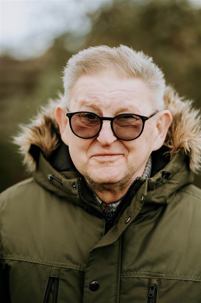 Portret van een oudere man in de natuur. Hij draagt een groene jas en draagt een bril
