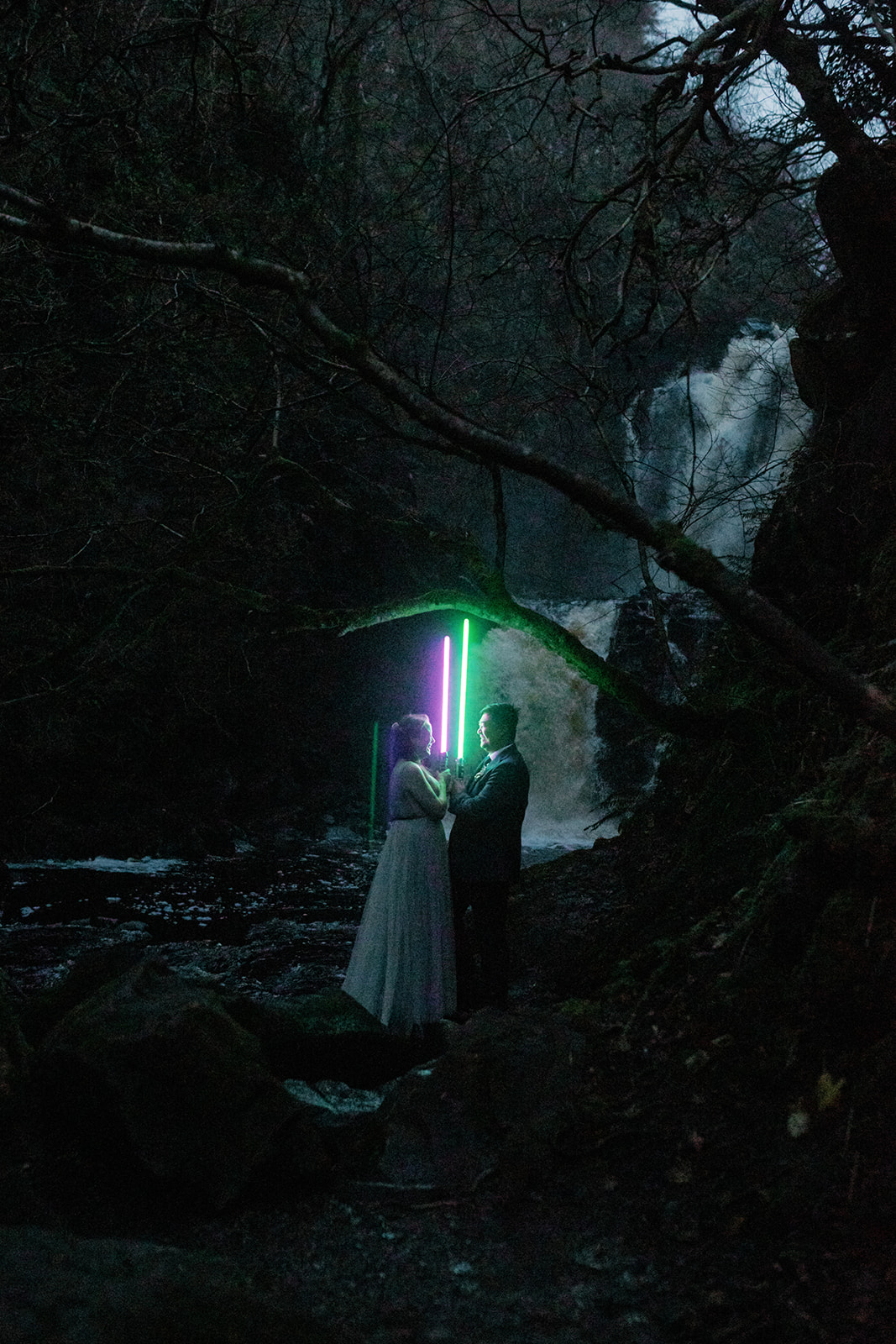 Mellie and Andrew pose for their evening Isle of Skye elopement photos while holding Star Wars light sabers as props.