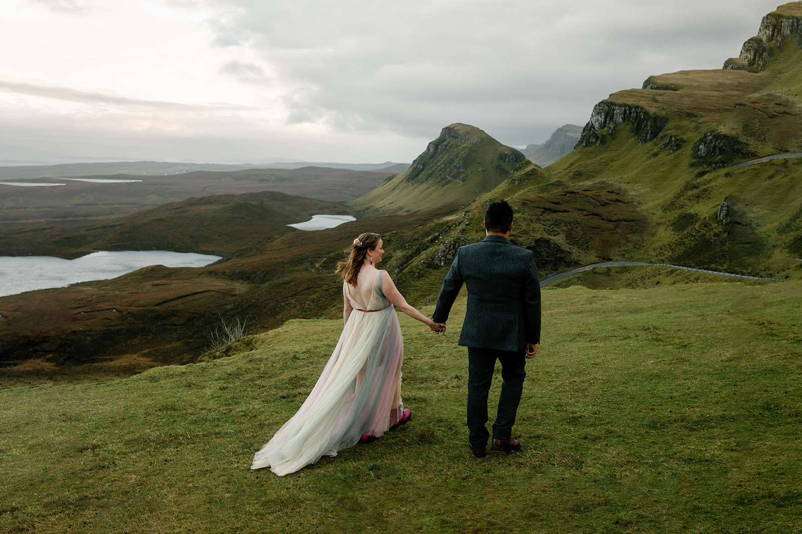 Mellie and Andrew stand hand in hand as they stare at the majestic view of Quiraing, Isle of Skye.
