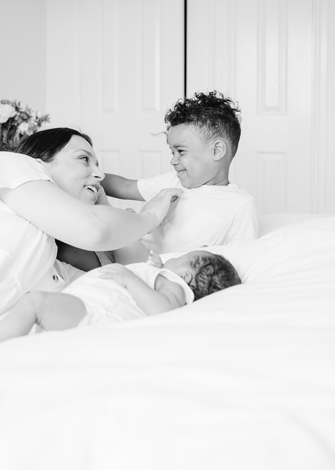 mum and sons playing on the bed together and laughing during the newborn baby photography at home in bristol