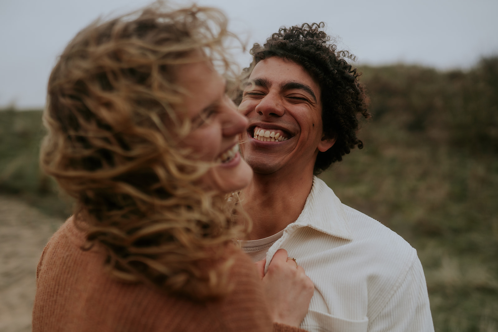 Steven laughing brightly with his brown curly hair in the dunes of netherlands