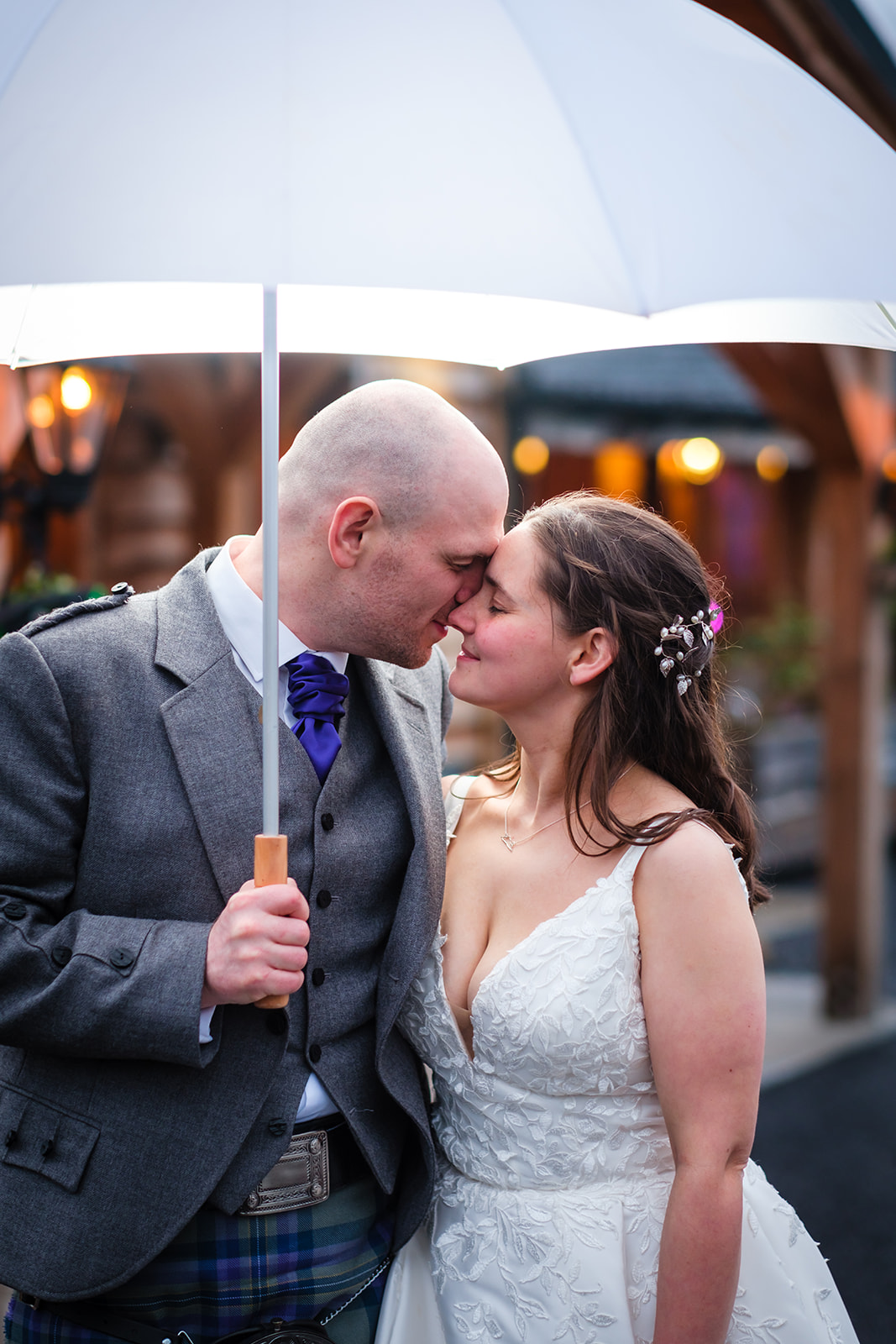 Bride and groom kiss underneath a white umbrella.