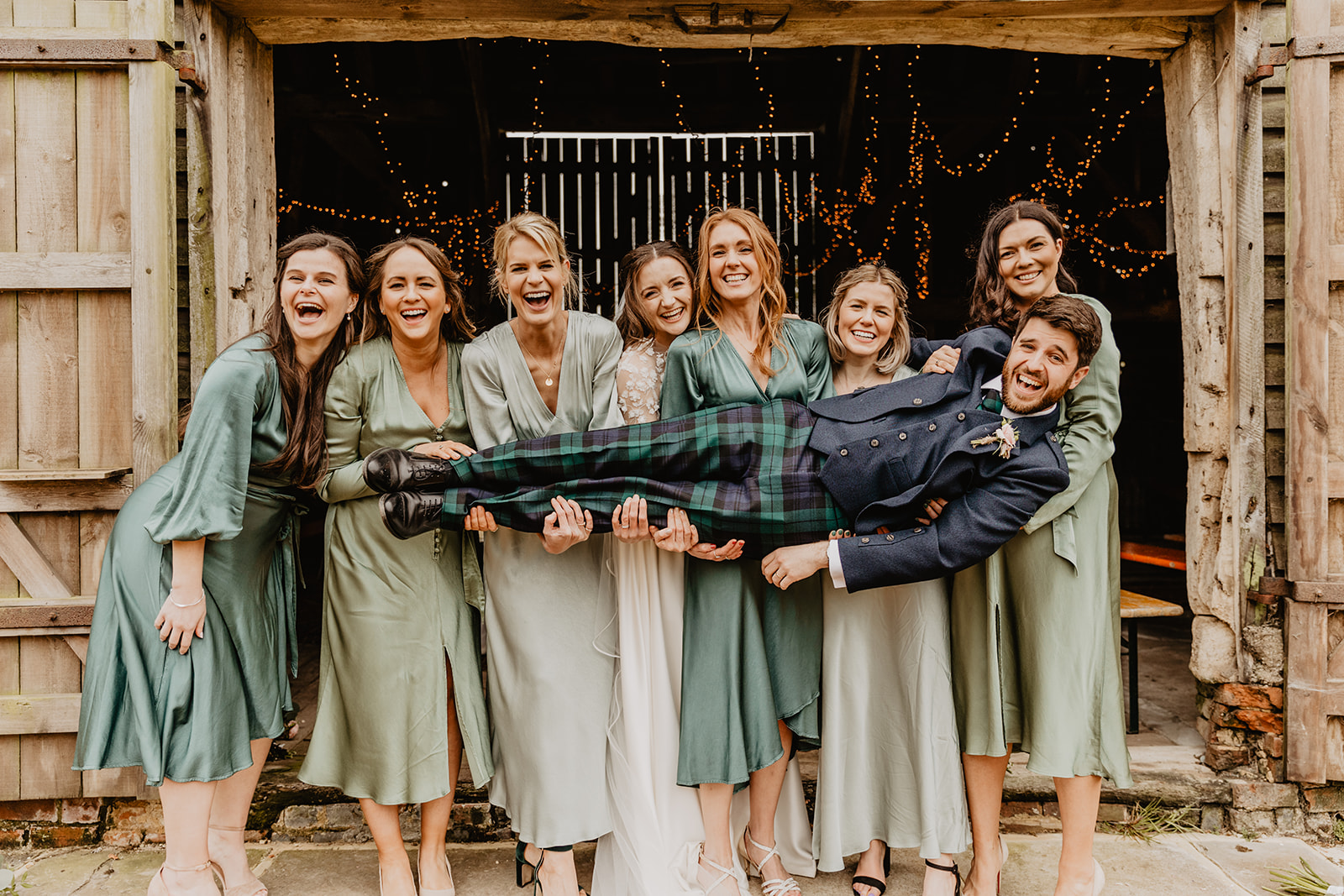 Bride and bridesmaids holding groom at a Secret Barn Wedding, West Sussex. By Olive Joy Photography