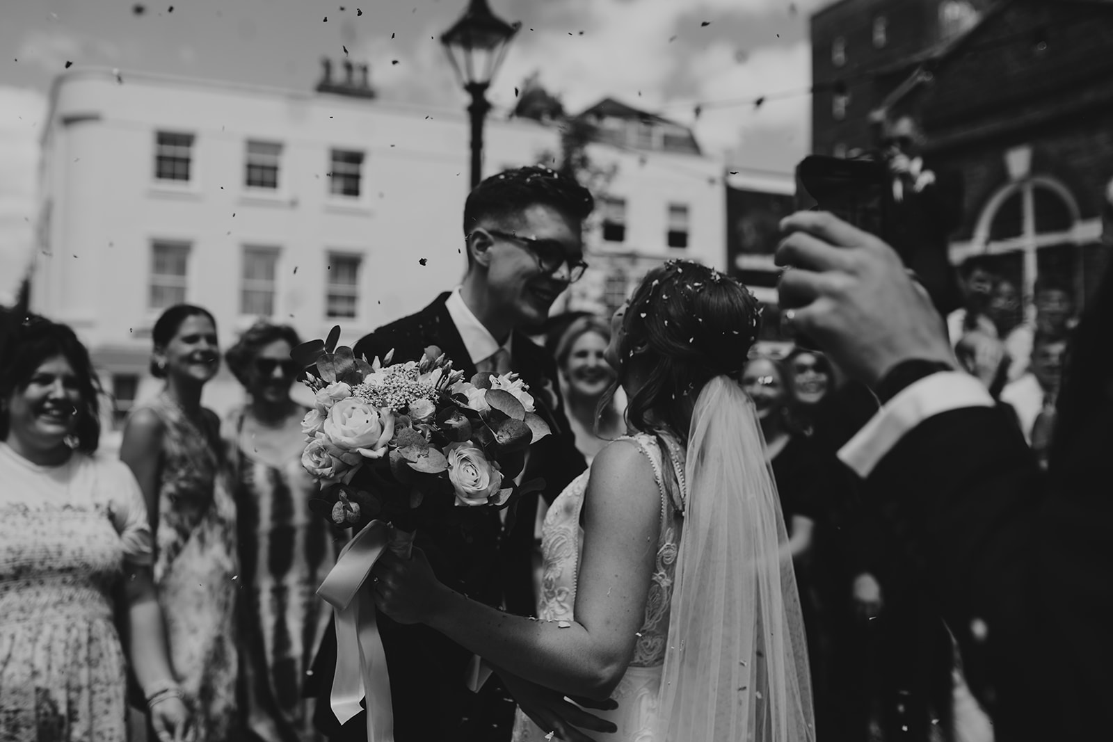 Black and white bride and groom smiling at each other during confetti tunnel at Surrey wedding 