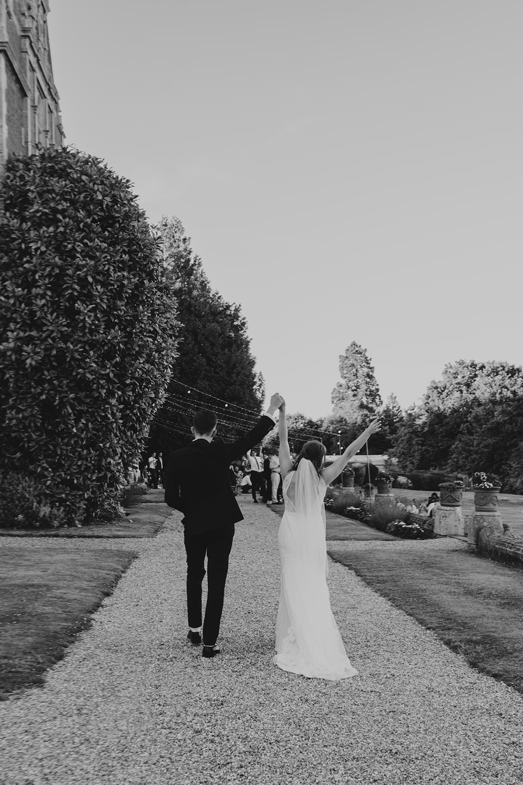 black and white of bride and groom walking towards guests with arms in the air at Surrey summer wedding 