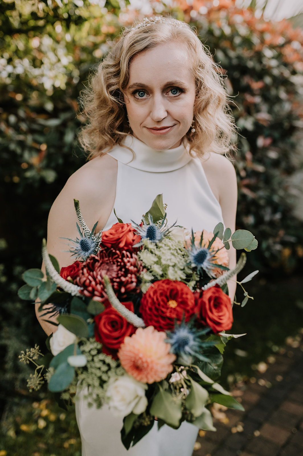 bride looking at camera holding red and orange flower bouquet in autumn Brighton wedding 
