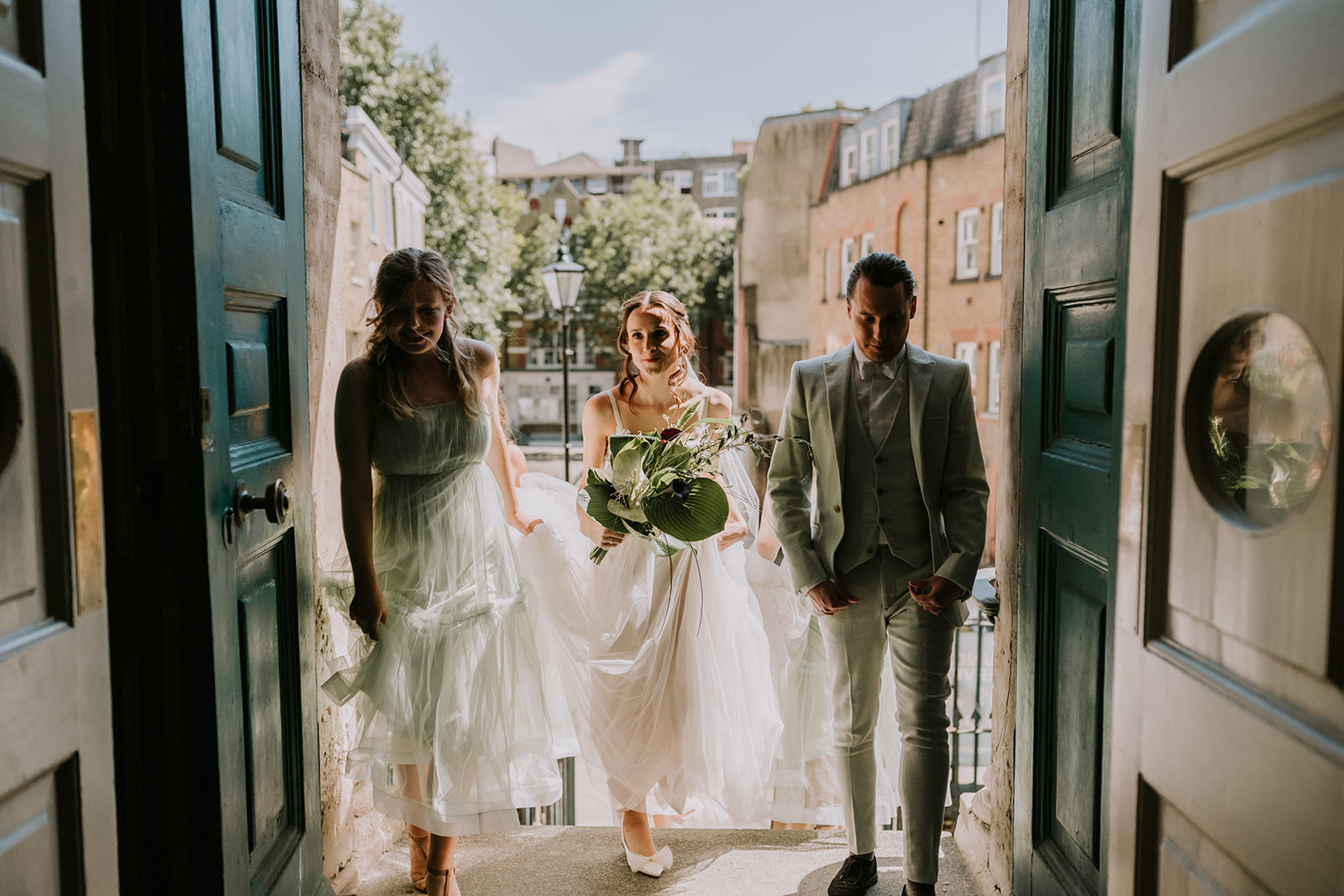 bride walking into crypt on green with bridesmaids in London wedding