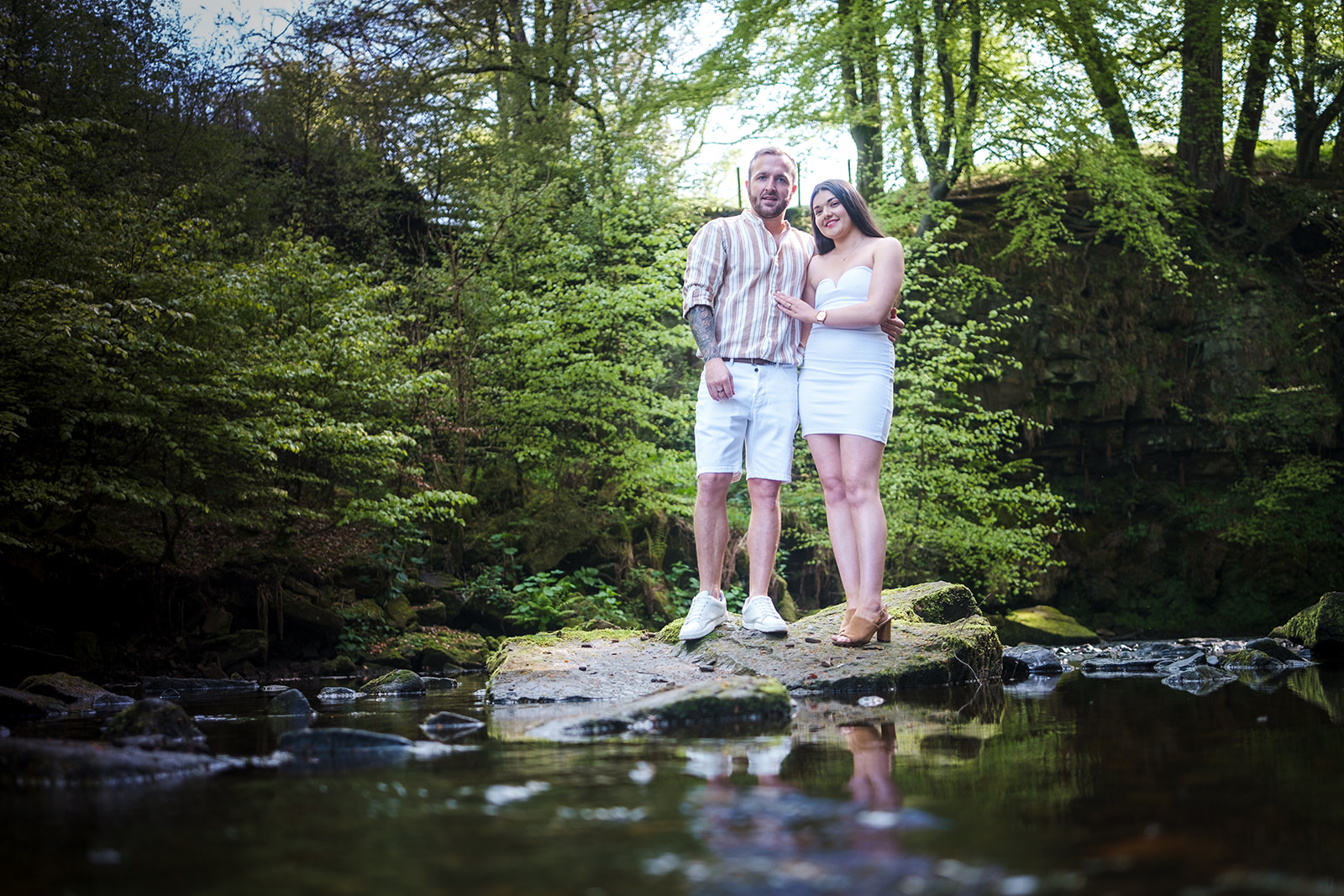 Engaged couple standing on a rock in the middle of a river with reflections in the water