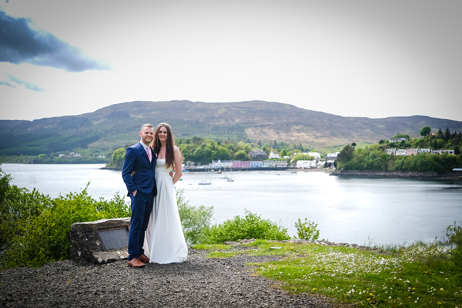The couple hugging with the Cullen hills and Portree harbour in the background