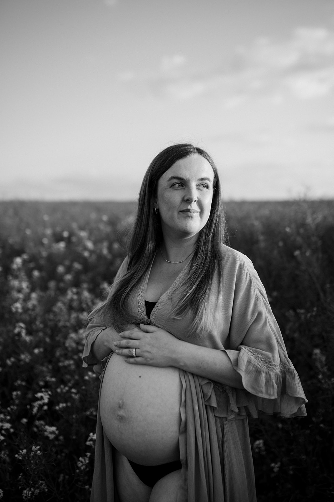 back and white image of expectant mother in a flower field at golden hour.
