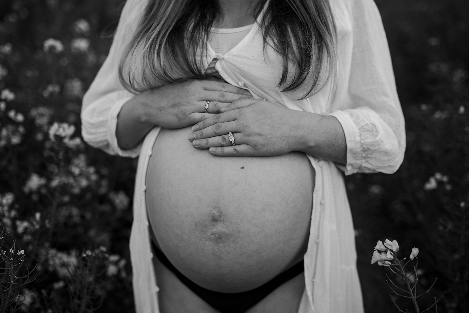 Black and white image of mother resting her hands on her bump during outdoor maternity shoot in a flower field in Devon.