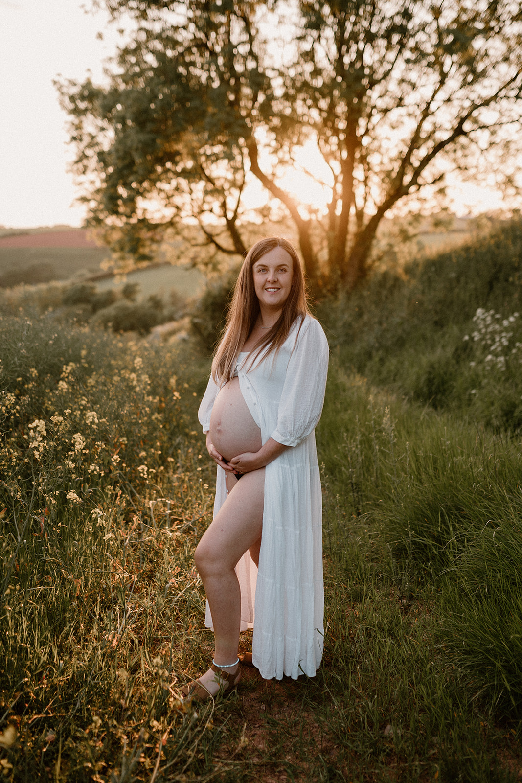Expectant mother cradles bump at sunset photo session.