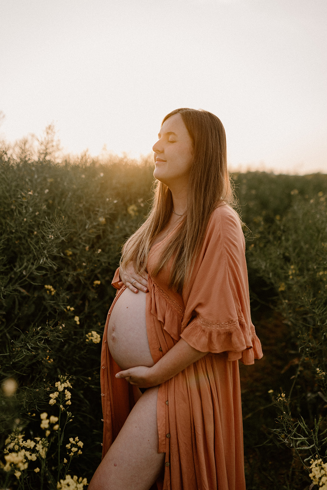 Expectant mother cradles bump during golden hour maternity photoshoot.