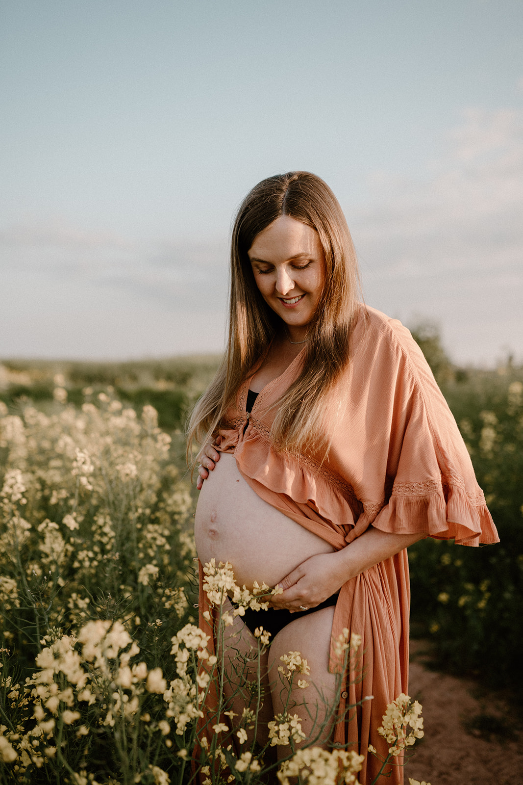 Mother looks at bump during outdoor maternity session at golden hour.