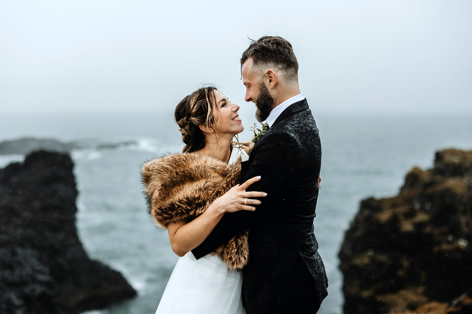 Married couple is hugging in Arnarstapi in front of the ocean and cliffs in Iceland