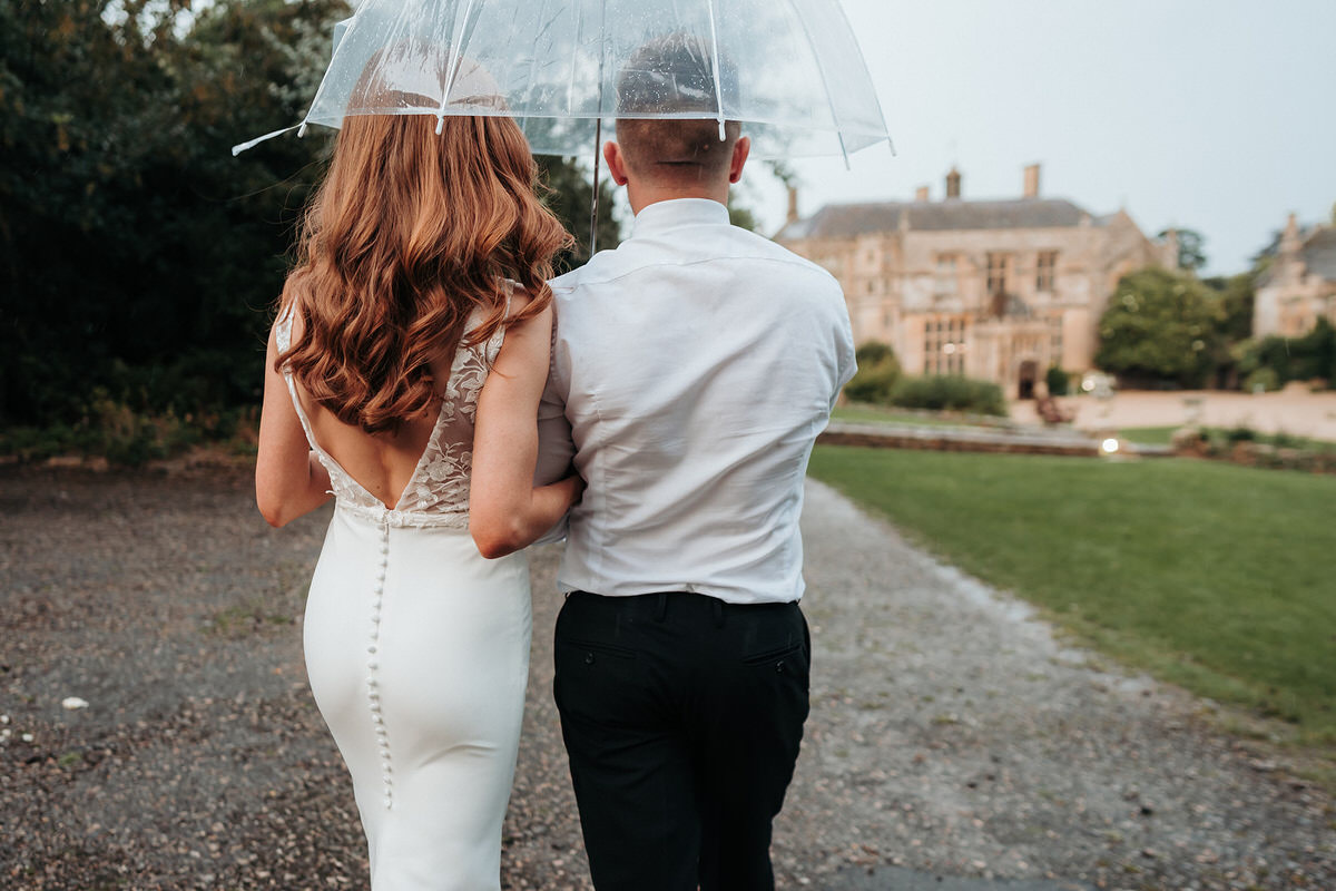 bride and groom walk with umbrella at Brympton House