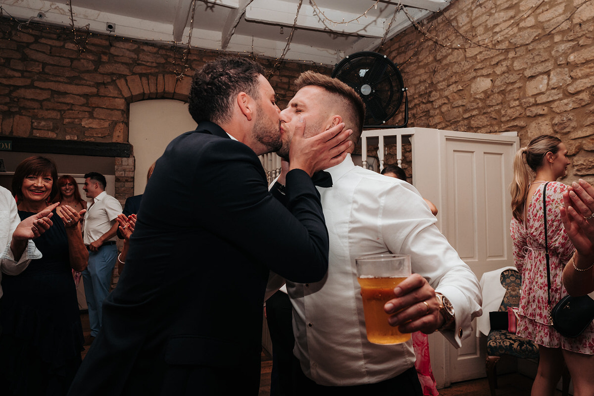 The groom kisses a male guest in the party barn 