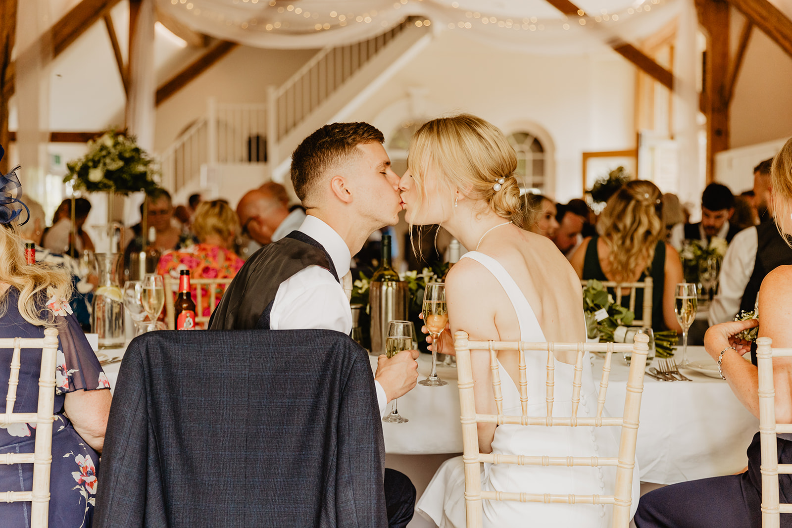 Bride and groom kissing at their table at a Bury Manor Barn Wedding in Sussex. Photographer OliveJoy Photography.
