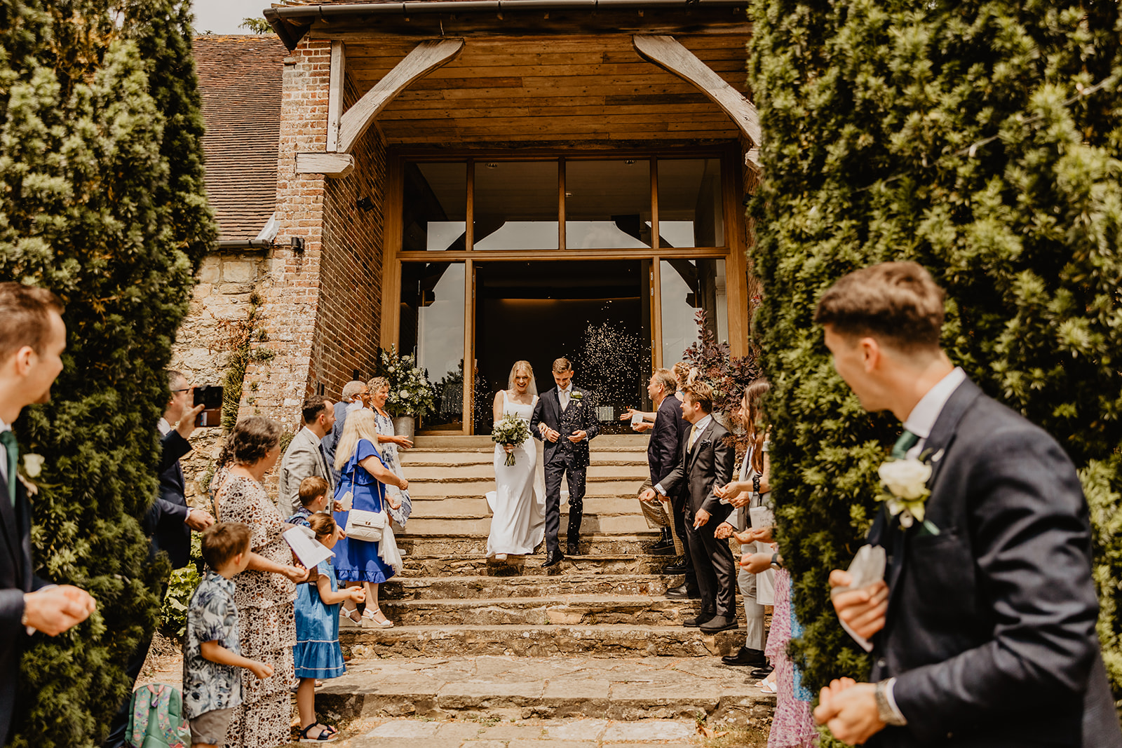 Bride and groom walking under confetti at a Bury Manor Barn Wedding in Sussex. Photographer OliveJoy Photography.