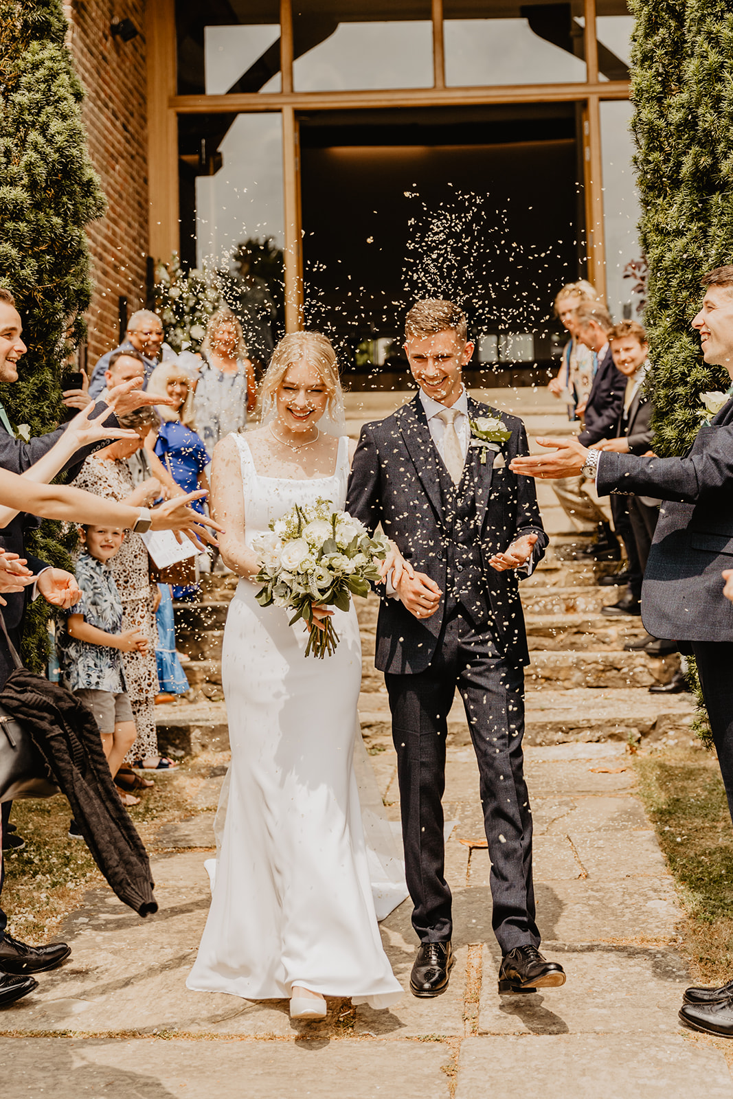 Bride and groom walking under confetti at a Bury Manor Barn Wedding in Sussex. Photographer OliveJoy Photography.