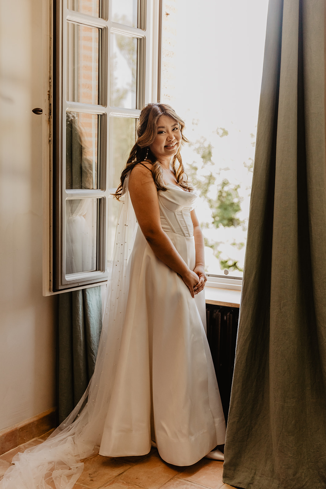 A bride by a villa window at a Destination Wedding in France. Photography & Videography by OliveJoy Photography