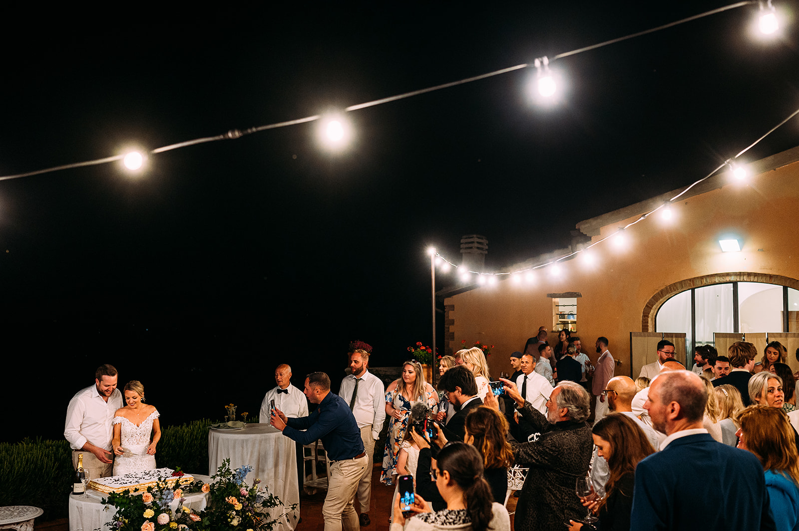 couple cutting the cake under the festoon bulbs at night