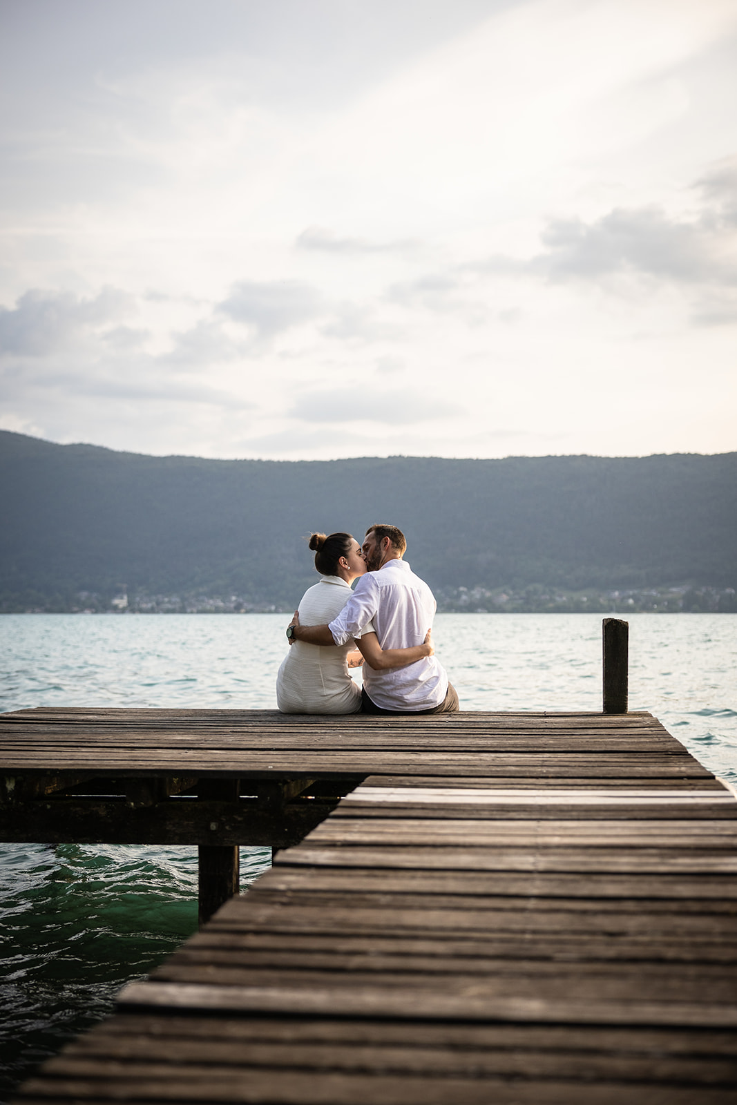 couple assis au bord du lac d'Annecy qui s'embrasse lors d'une séance photo avec un photographe professionnel