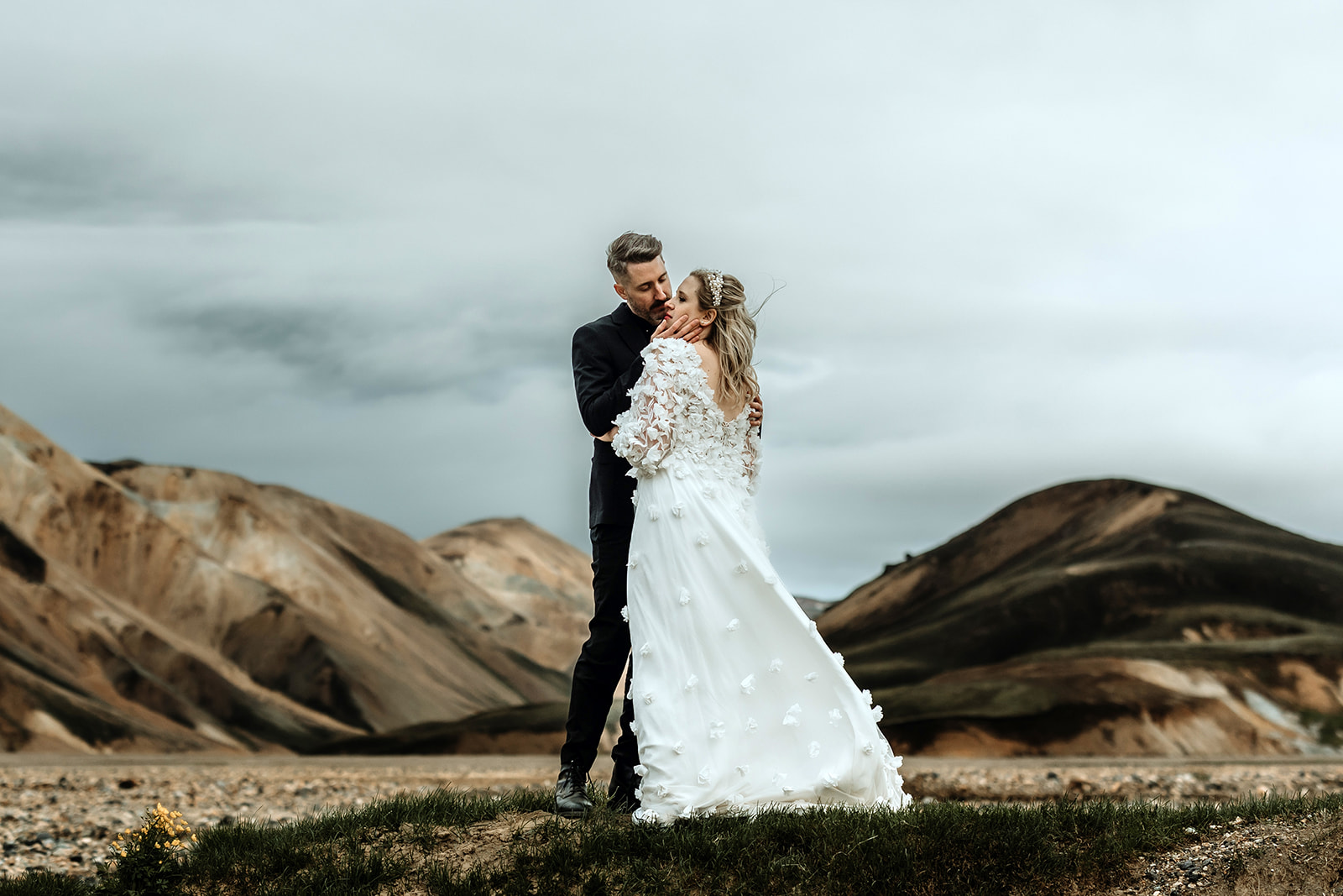 Married couple in wedding attire embracing tightly in the dramatic and moody landscape of the Icelandic highlands,
