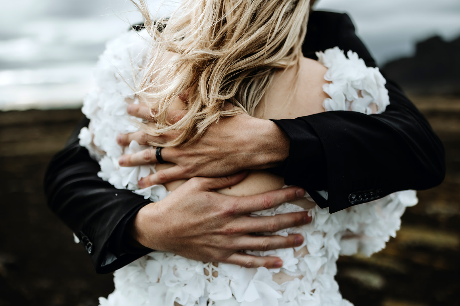 Close-up of a groom holding his bride tightly from behind, with a focus on their interlocked hands in Iceland