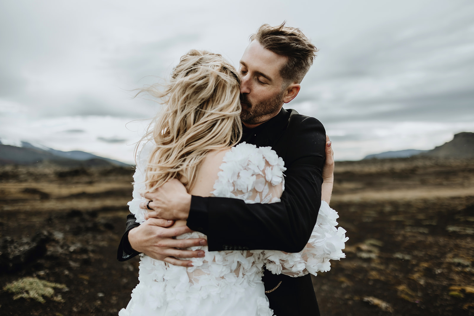 Close-up of a groom holding his bride tightly from behind, with a focus on their interlocked hands in Iceland