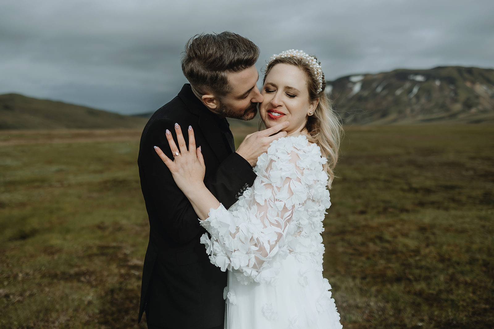 Married couple in wedding attire embracing tightly in the dramatic and moody landscape of the Icelandic highlands,