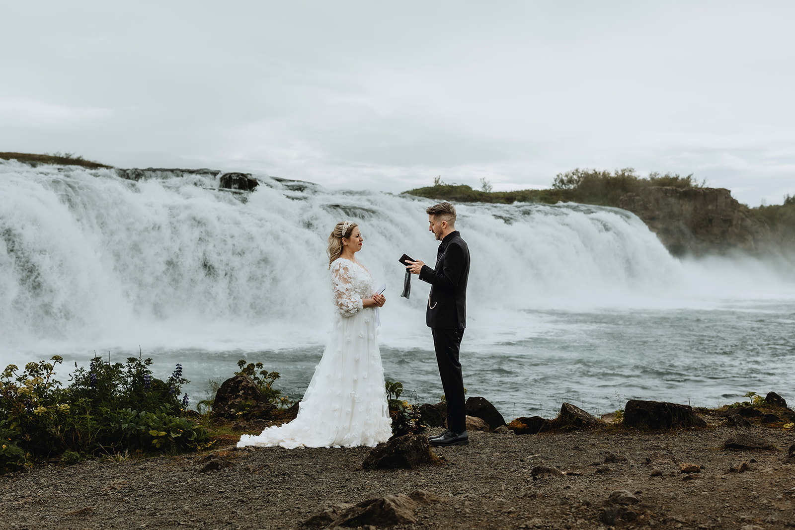Waterfall ceremony in Iceland. Bride and groom are standing in front of a waterfall and exchanging their vows.