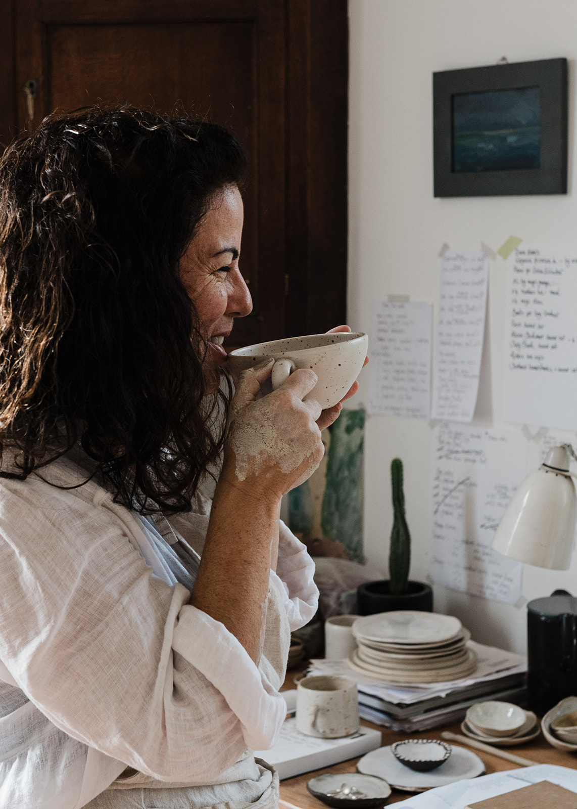 Portrait of woman drinking from a handmade pottery mug in her ceramics studio.