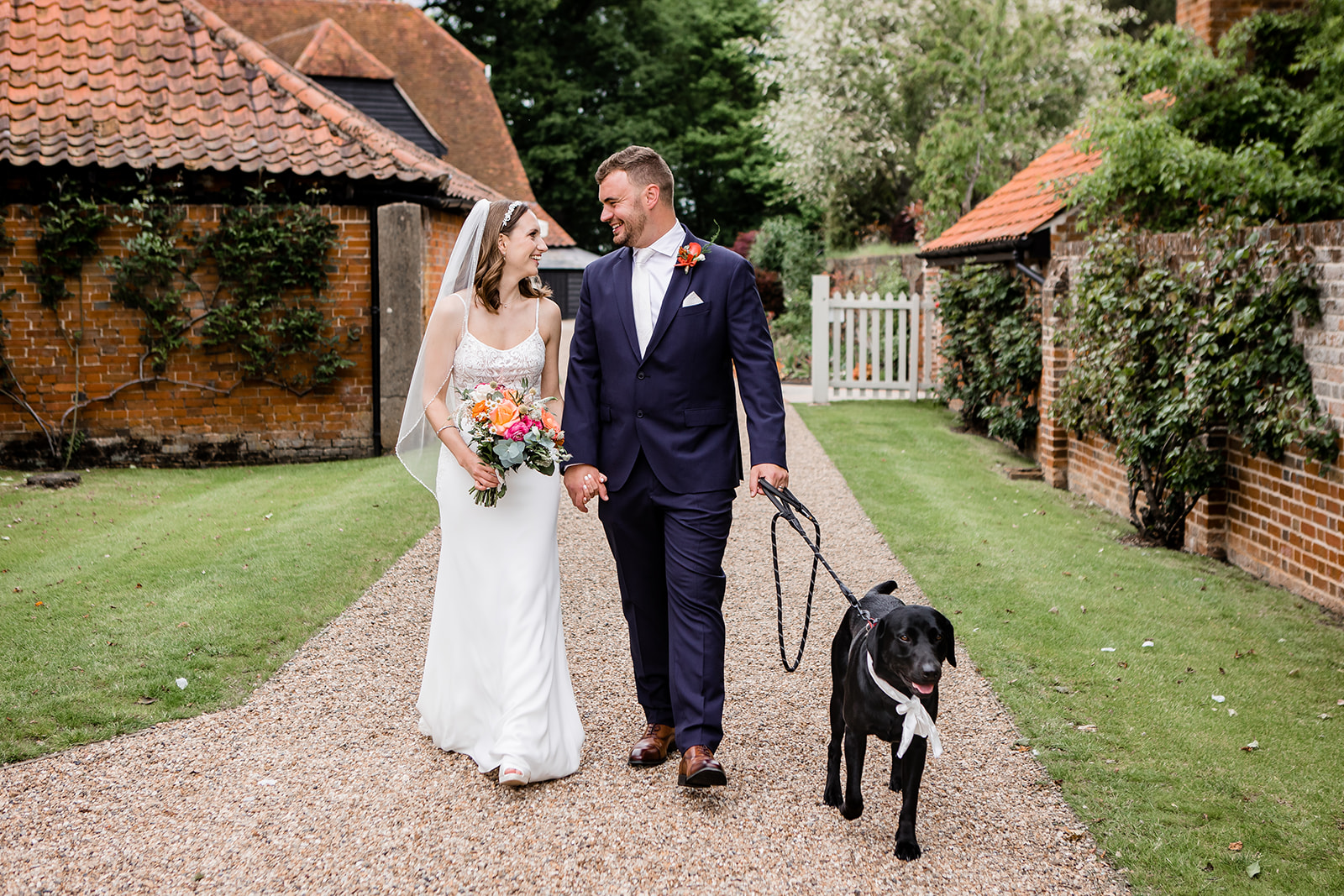 The wedding couple and their dog walking to the secret garden at Blake Hall