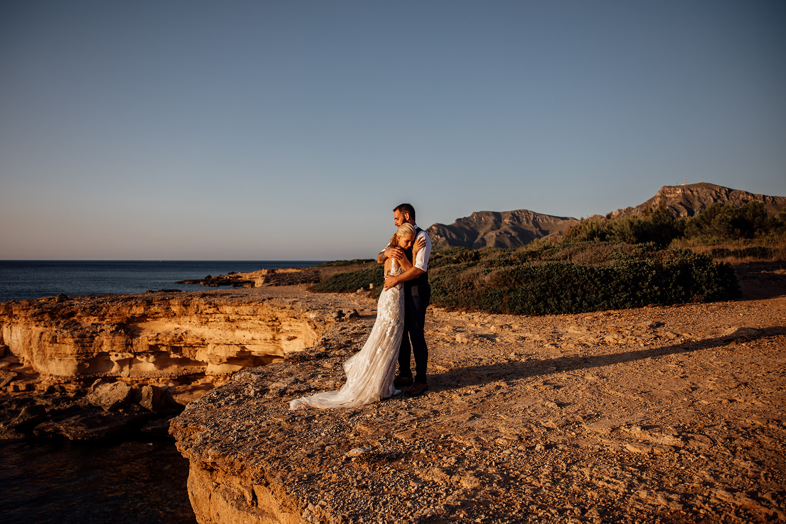 After Wedding Shooting Mallorca - Paar steht am Meer - Sonne im Hintergrund 
