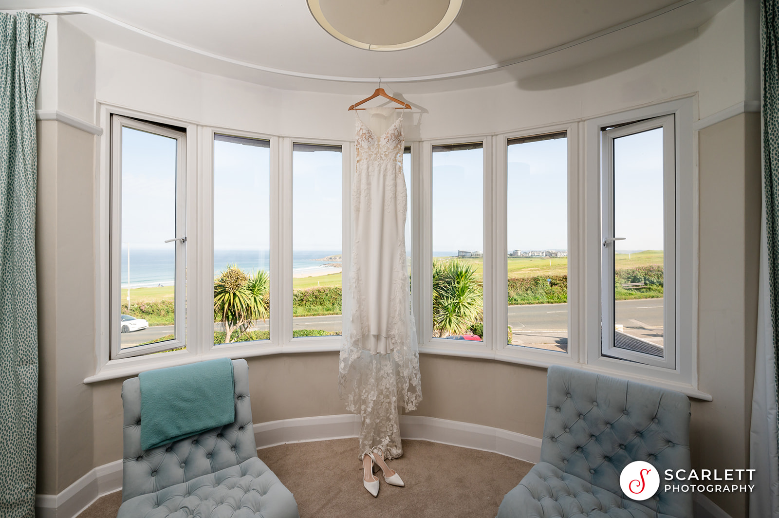 Wedding dress hanging from panoramic windows overlooking Fistral beach
