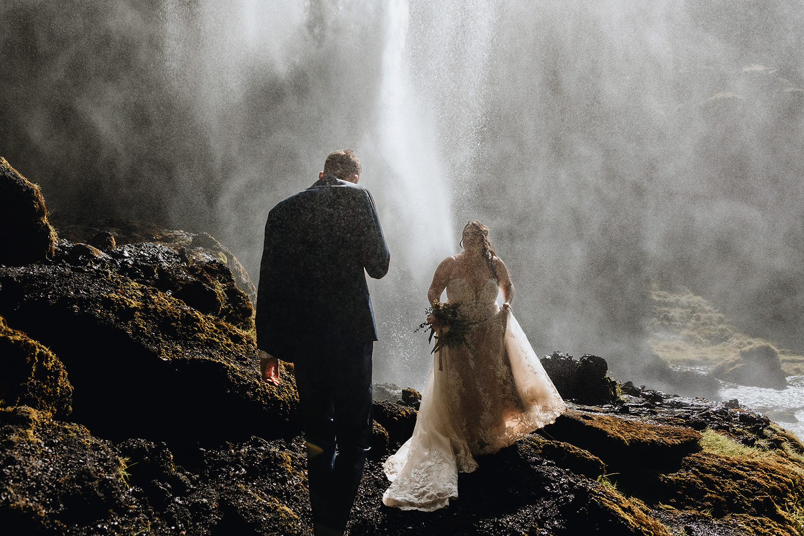 Newlywed couple is behind a waterfall on the south coast of Iceland on their wedding day