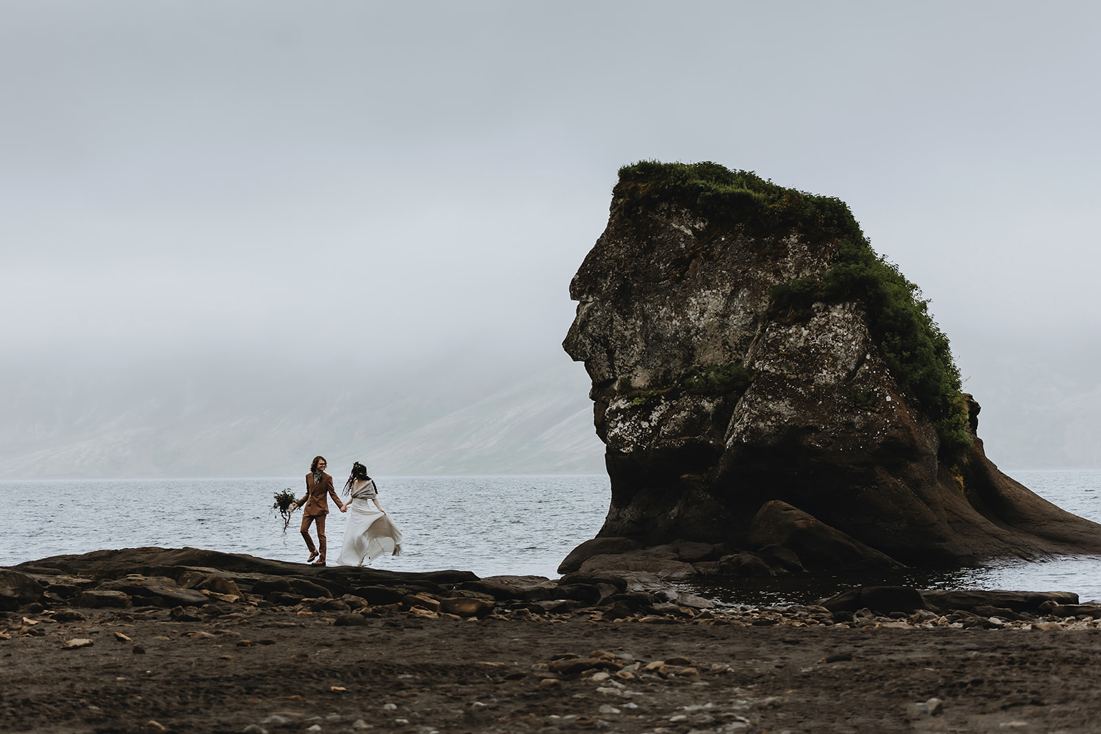 Newlywed couple is having fun on the Reykjanes Peninsula in front of a huge cliff