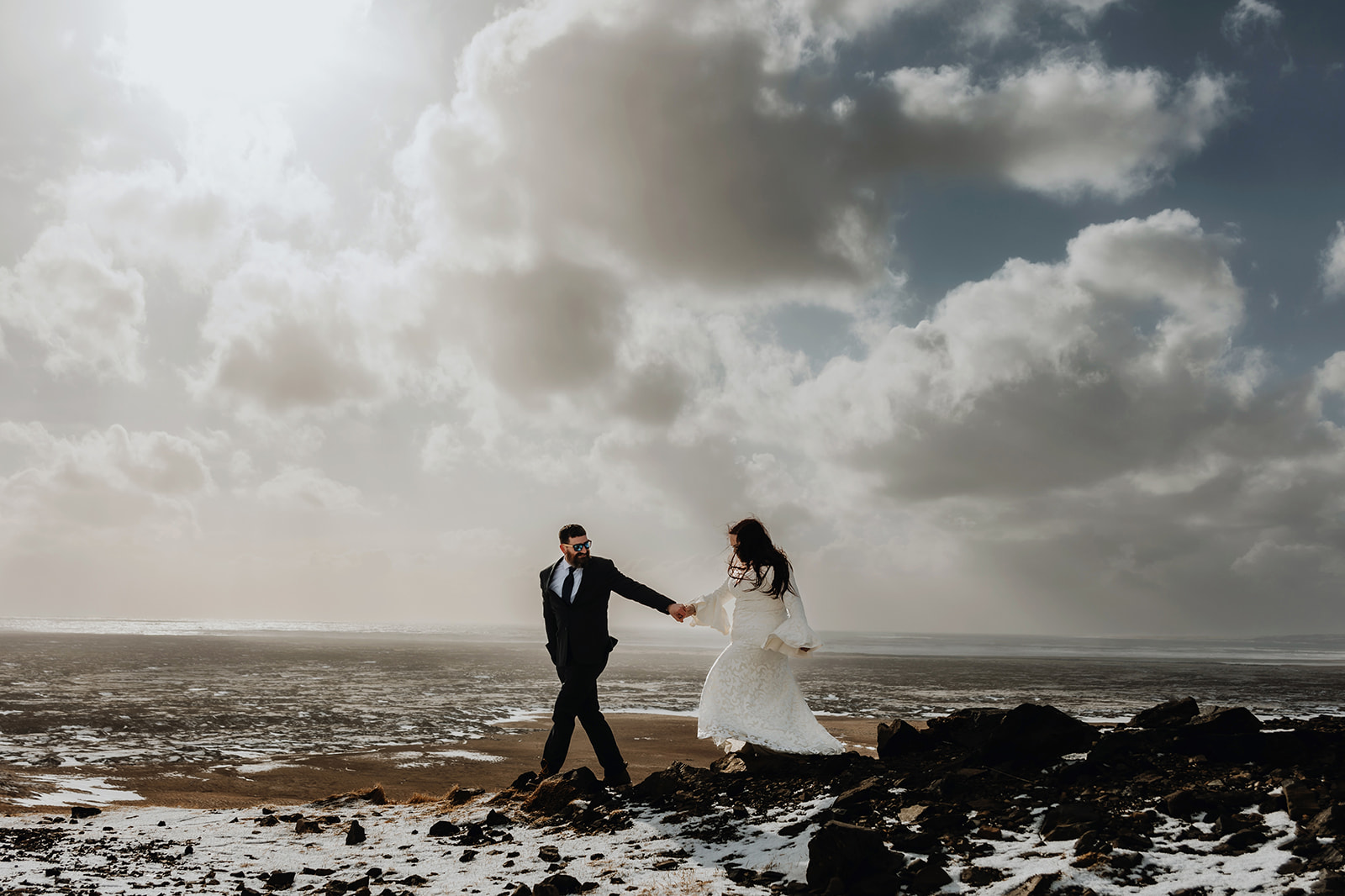 Bride and groom is holding hands in a snowy landscape with dramatic clouds on their elopement in Iceland