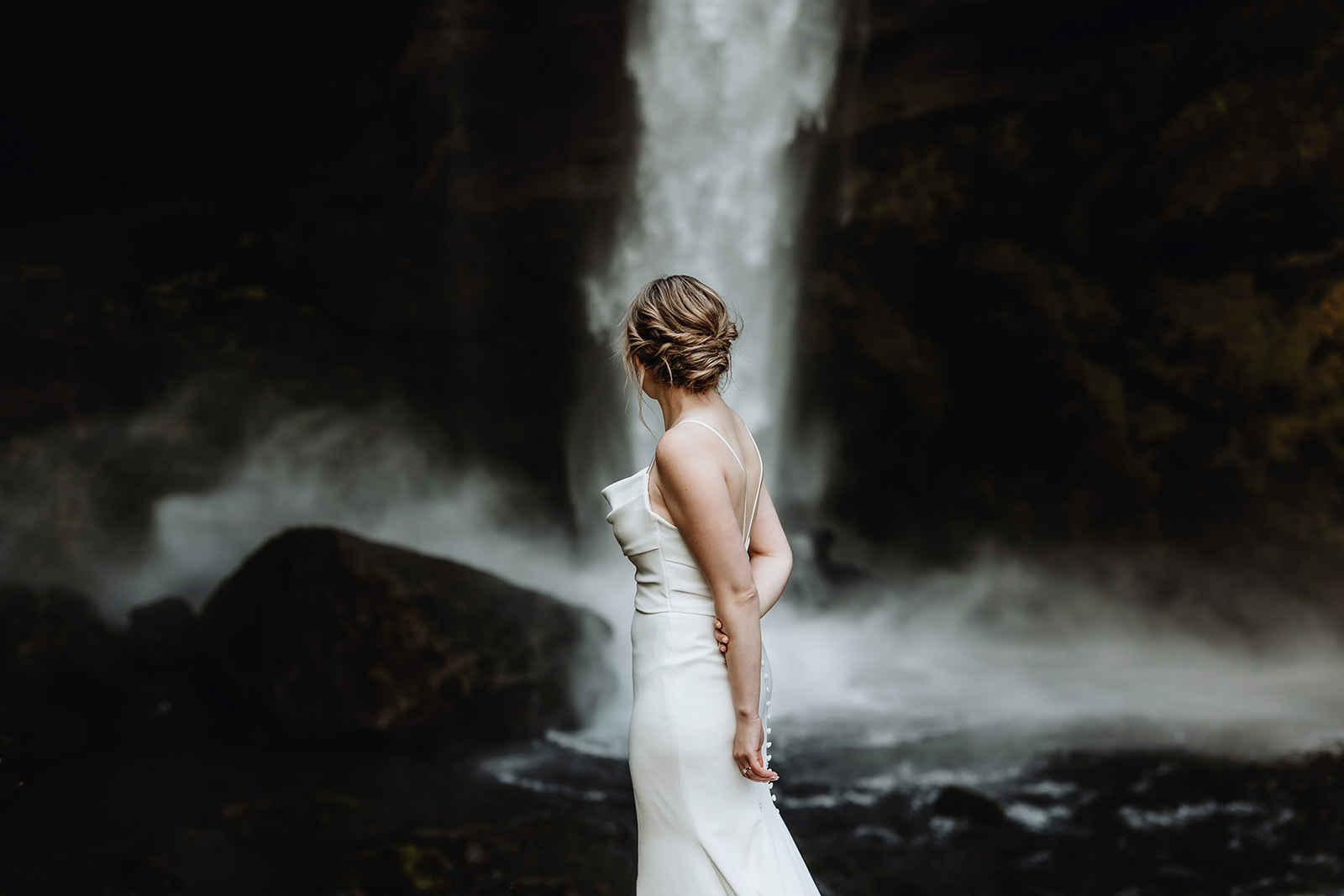 Elegant and Modern bride is looking at a waterfall in Iceland.