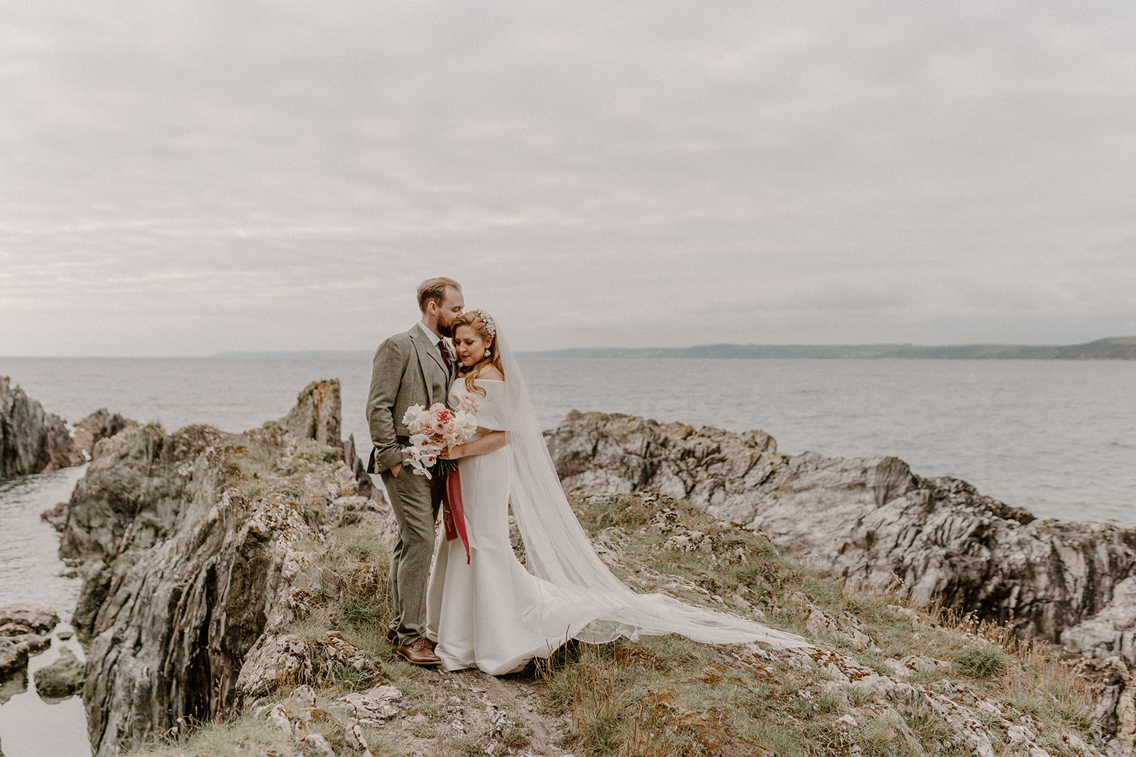 Bride and groom on rocks overlooking sea at Polhawn Fort