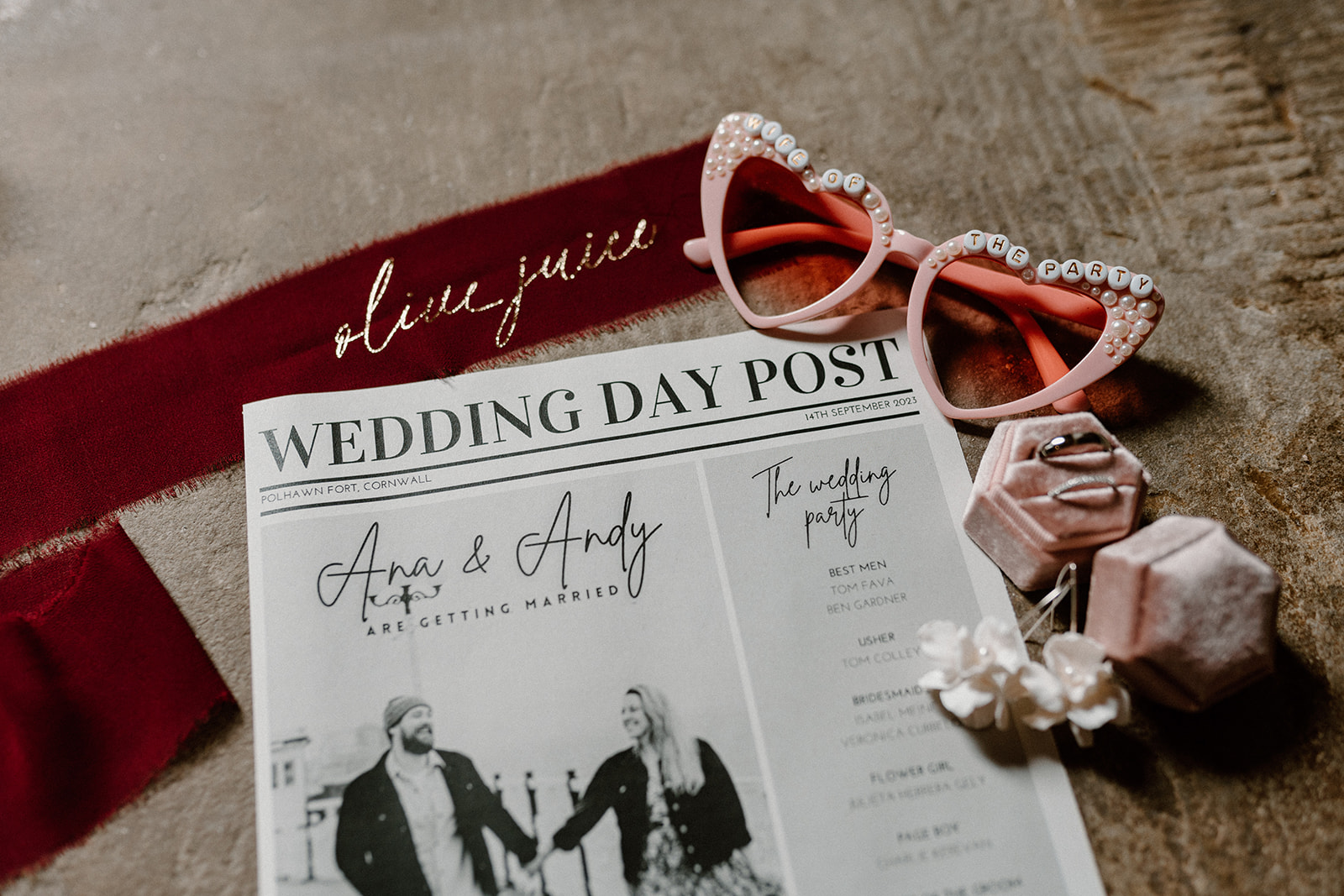 Flat lay of bridal details including wedding day newspaper, sunglasses, rings and ribbon
