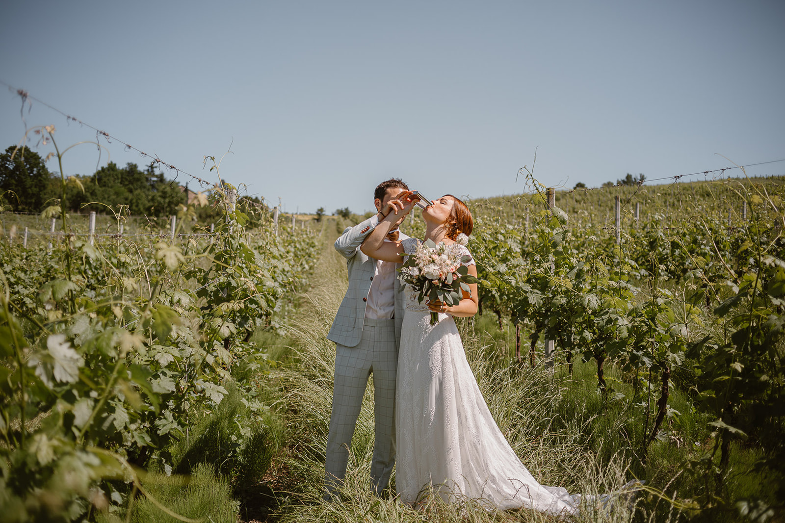 Couple photo in the vineyard of bride and groom drinking alchool froma little bottle