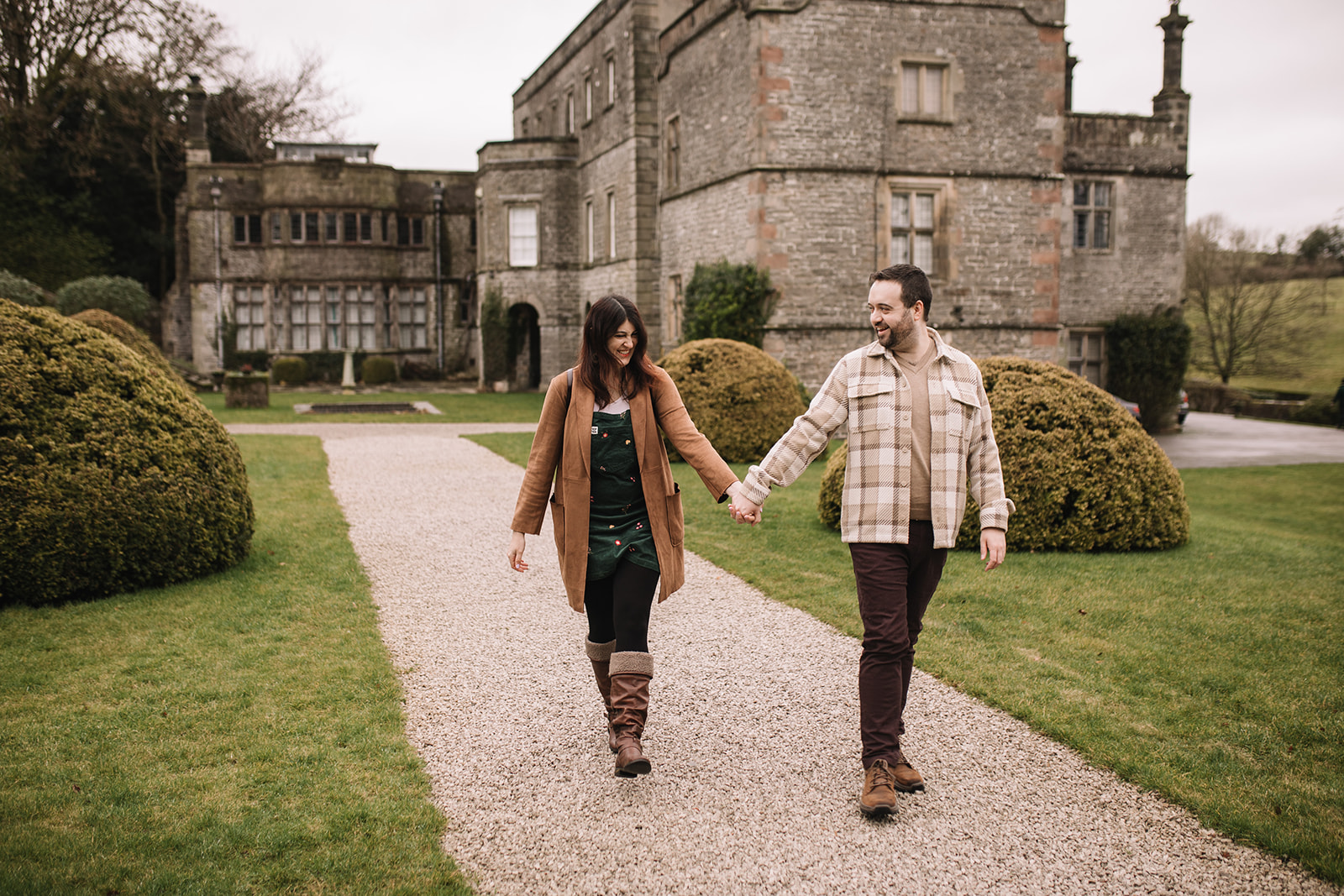 A couple walking and laughing in the grounds of Tissington Hall with the Hall in the background