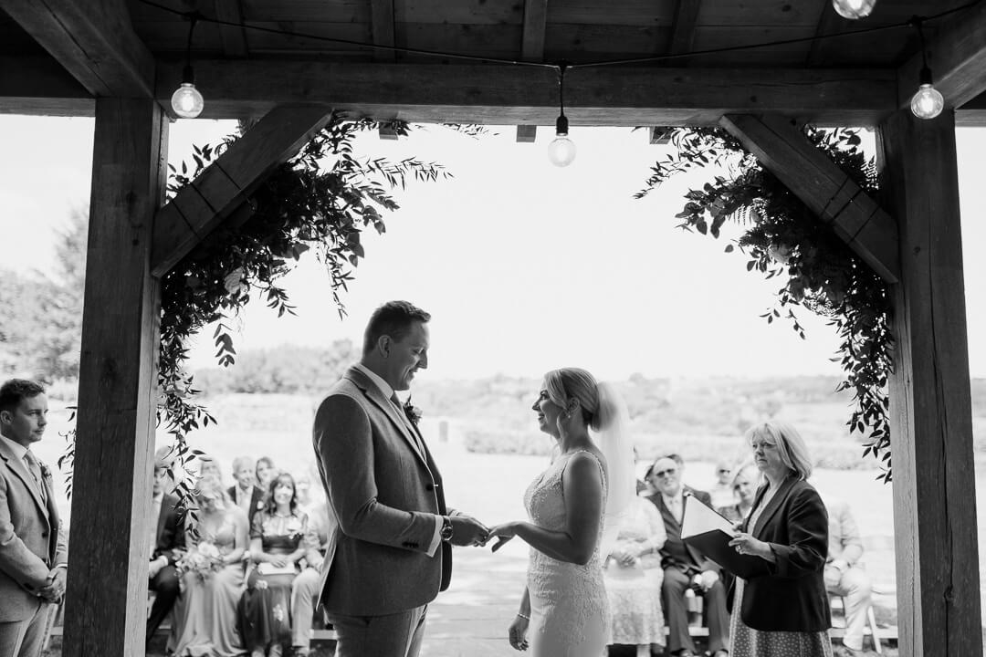 Bride and groom exchange weddings rings under the arbour at Trevenna Barns.