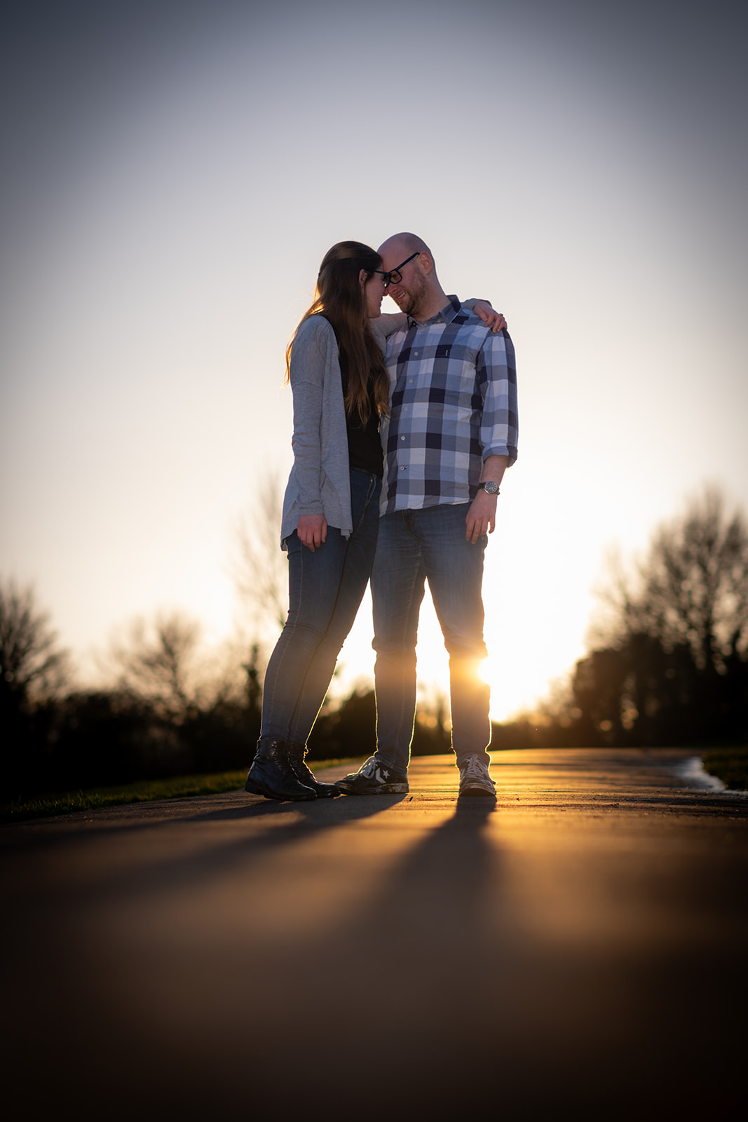 A couple stand closely together as the sun sets behind them as their engagement shoot comes to an end
