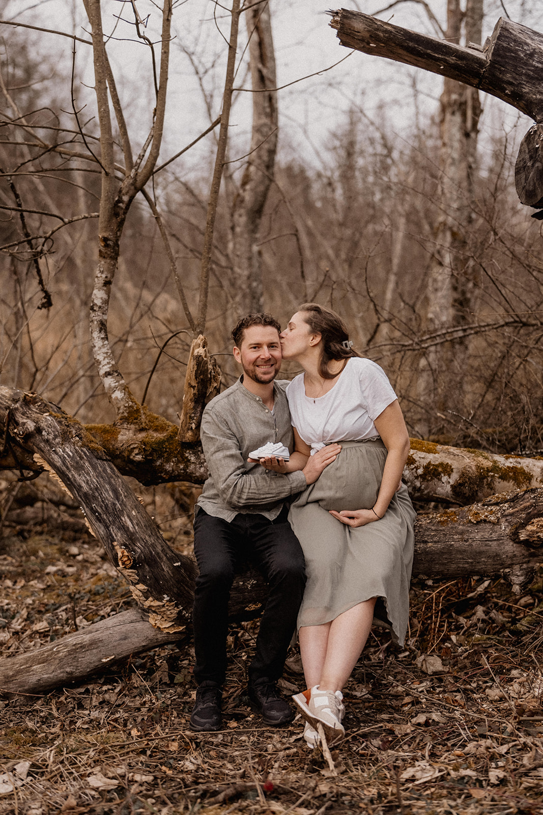 Sitzendes Paar mit schwangerer Frau bei Babybauchshooting in der Natur